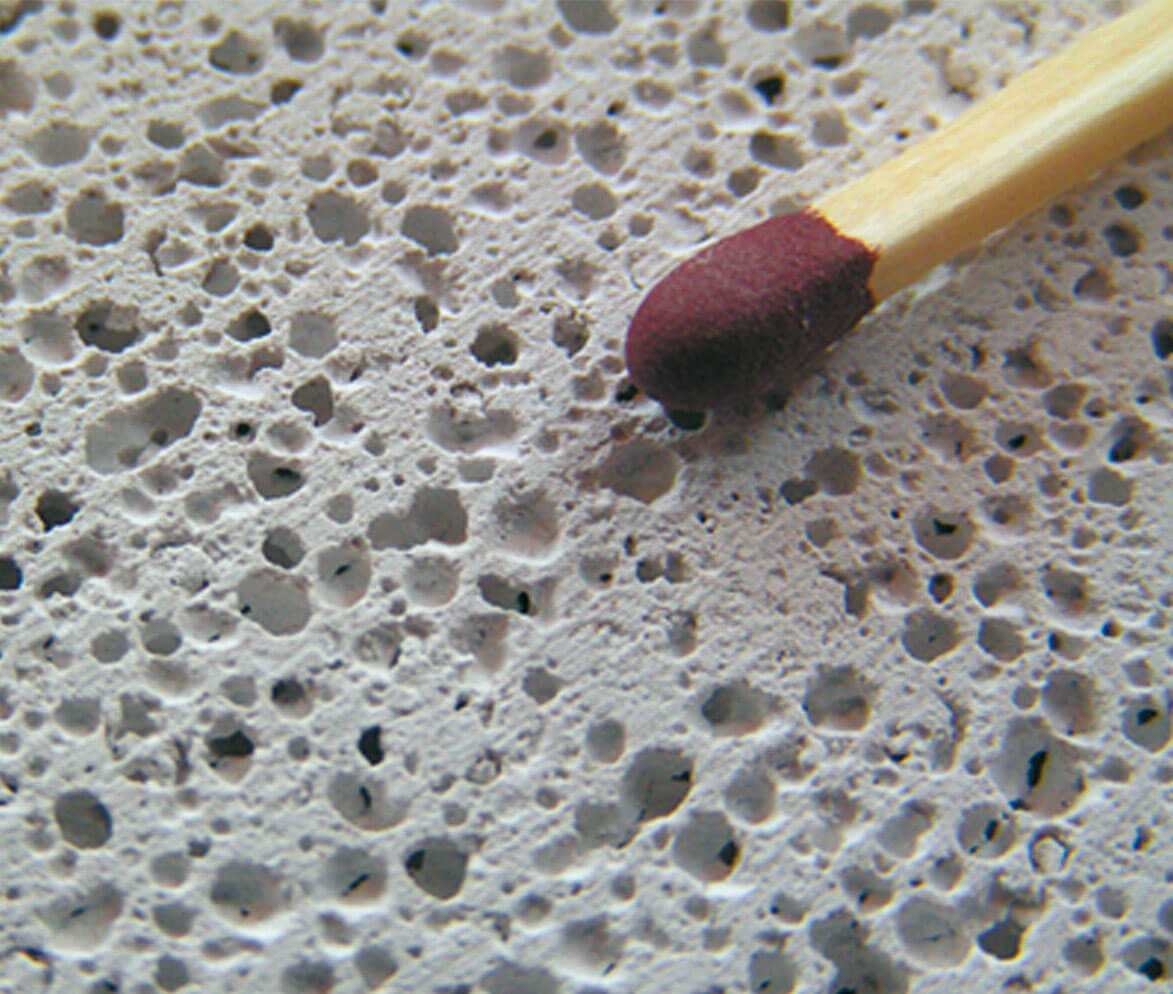 Eine Nahaufnahme von einem Streichholzkopf auf grauem Porenbeton (l?chrige Oberfl?che).